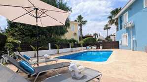 Una piscina con sillas de descanso y una sombrilla, rodeada por una valla y follaje.