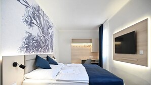 Una camera d'albergo con un letto, un comodino, una TV a parete e un'area scrivania con una sedia.