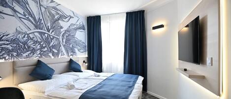 Una habitación de hotel moderna con una cama grande, un televisor de pantalla plana en la pared y una obra de arte floral de gran tamaño.