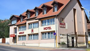 Un hotel con un tetto in tegole rosse, numerose finestre e un cartello con la scritta "MERLOT HOTEL".