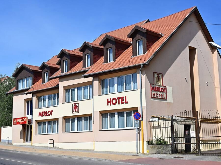A hotel with a red-tiled roof, multiple windows, and a sign reading "MERLOT HOTEL".