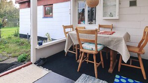 Un patio techado con una mesa y sillas, una lámpara colgante y vistas a una casa con ventana.