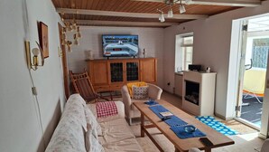 Un salón acogedor con techo de madera, un televisor montado en la pared, un sofá, una mesa con individuales y una chimenea.