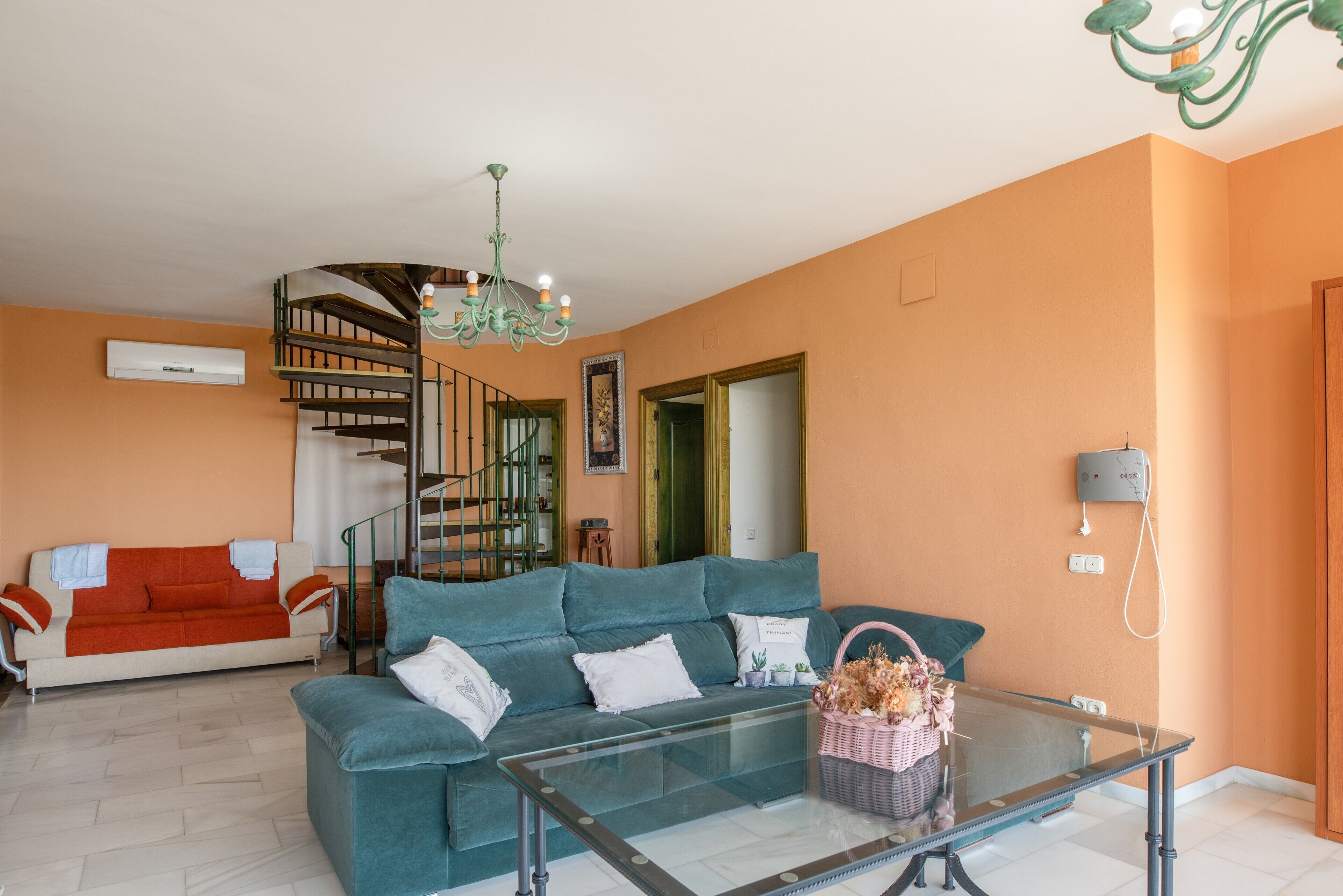 Una sala de estar con un sofá color turquesa, una mesa de centro de vidrio, una escalera y una araña.