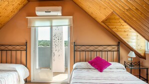 A bedroom with a sloped ceiling, a bed with a striped bedspread, a pink pillow, a nightstand with a lamp, and a sliding glass door leading to an outdoor area.