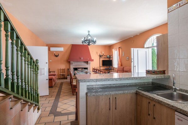 Una cocina con una isla central, comedor y escalera.
