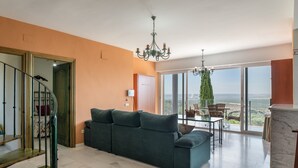 A spacious living area with a sofa, a dining table, and chairs, a staircase, and large windows offering a view.