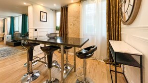A modern kitchen with a bar area, a dining table, and a large clock on the wall. - UrbanFlat 113 - Groundfloor Apartment Paris Historic Center (París)