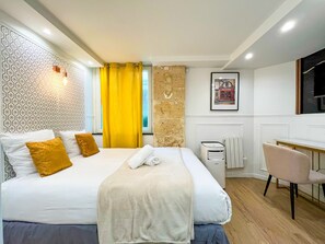 A hotel room with a bed, a desk, a chair, a radiator, and a patterned wall. - UrbanFlat 113 - Groundfloor Apartment Paris Historic Center (París)
