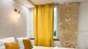 A hotel room with a patterned wall, a bed with white and brown pillows, a yellow curtain, and a view through a window. - UrbanFlat 113 - Groundfloor Apartment Paris Historic Center (París)