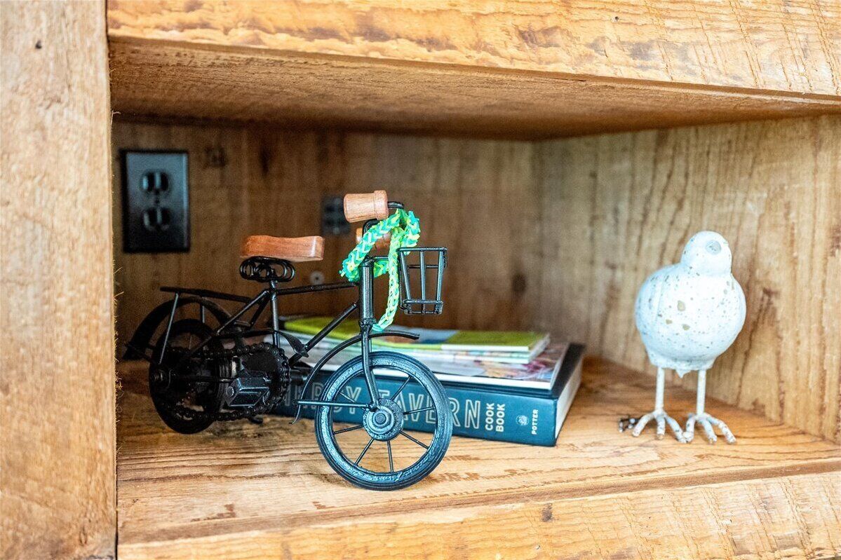 A wooden shelf with a small black bicycle, a green and white object, and a white bird figurine.