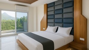 A modern bedroom with a large bed, a wooden headboard, and a balcony with a mountain view. - HOTEL KARDHAR INN (Ambaji)