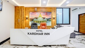 A hotel reception desk with a wooden panel design, a large framed picture of a building, and two leather chairs. - HOTEL KARDHAR INN (Ambaji)