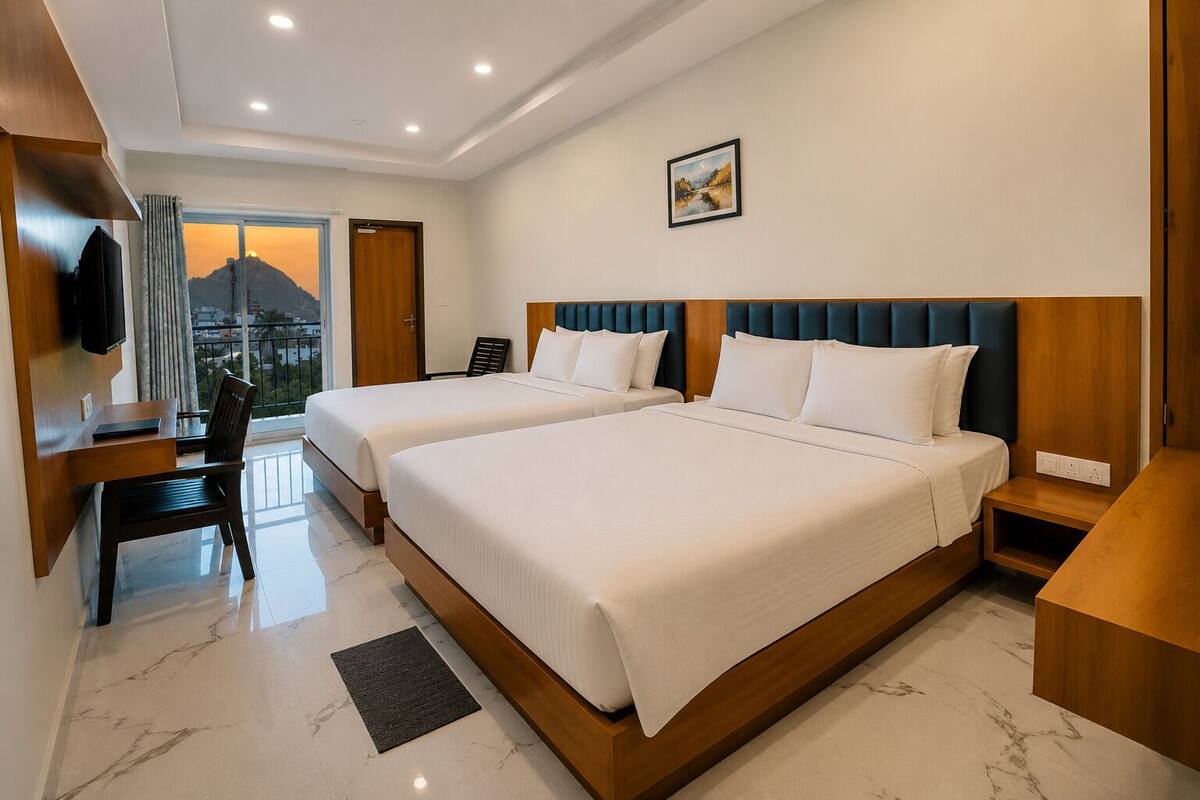 A hotel room with two beds, a desk, a chair, a TV, and a view of a mountain.