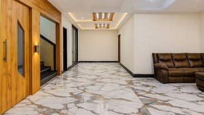 A hallway with a marble floor, wooden doors, and a brown leather sofa. - HOTEL KARDHAR INN (Ambaji)