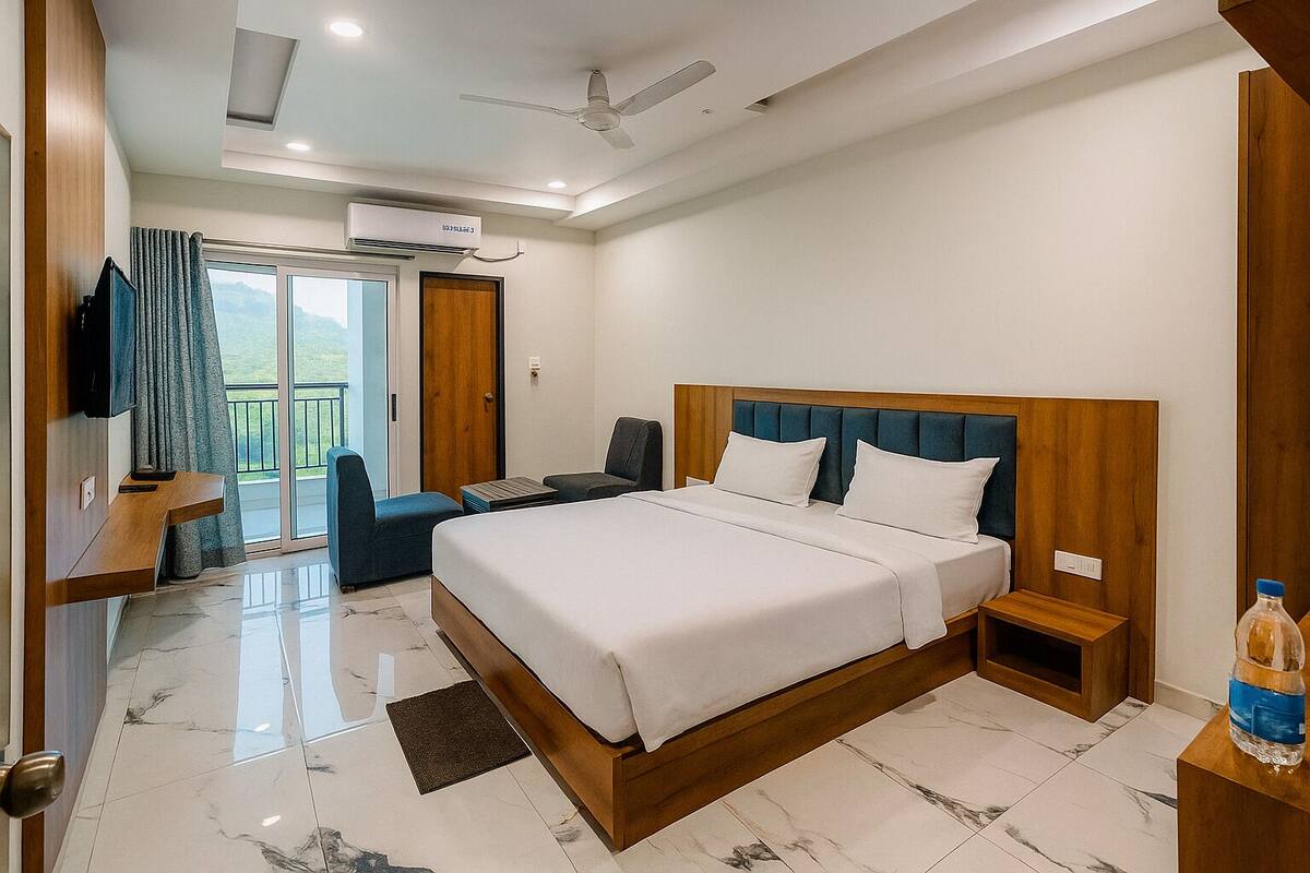 A modern hotel room with a large bed, a TV, a balcony with a view, and a ceiling fan.