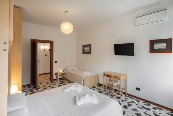 A hotel room with a bed, bedside table, chair, wall-mounted TV, and an air conditioning unit.