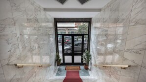 A marble staircase leading to a black-framed entrance with a red carpet, potted plants, and a view of parked cars outside. - 323 Cilea Apartment (Napoli)