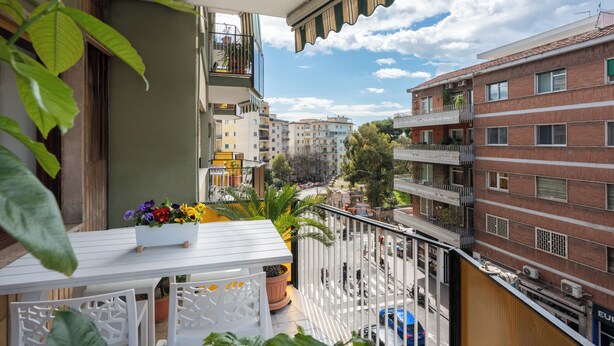 A balcony with a white table, potted plants, and a view of surrounding buildings. - 323 Cilea Apartment (Napoli)