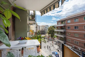 A balcony with a white table, potted plants, and a view of surrounding buildings.
