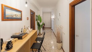 A hallway with a reception desk, chairs, a potted plant, framed artwork, and a door. - 323 Cilea Apartment (Napoli)