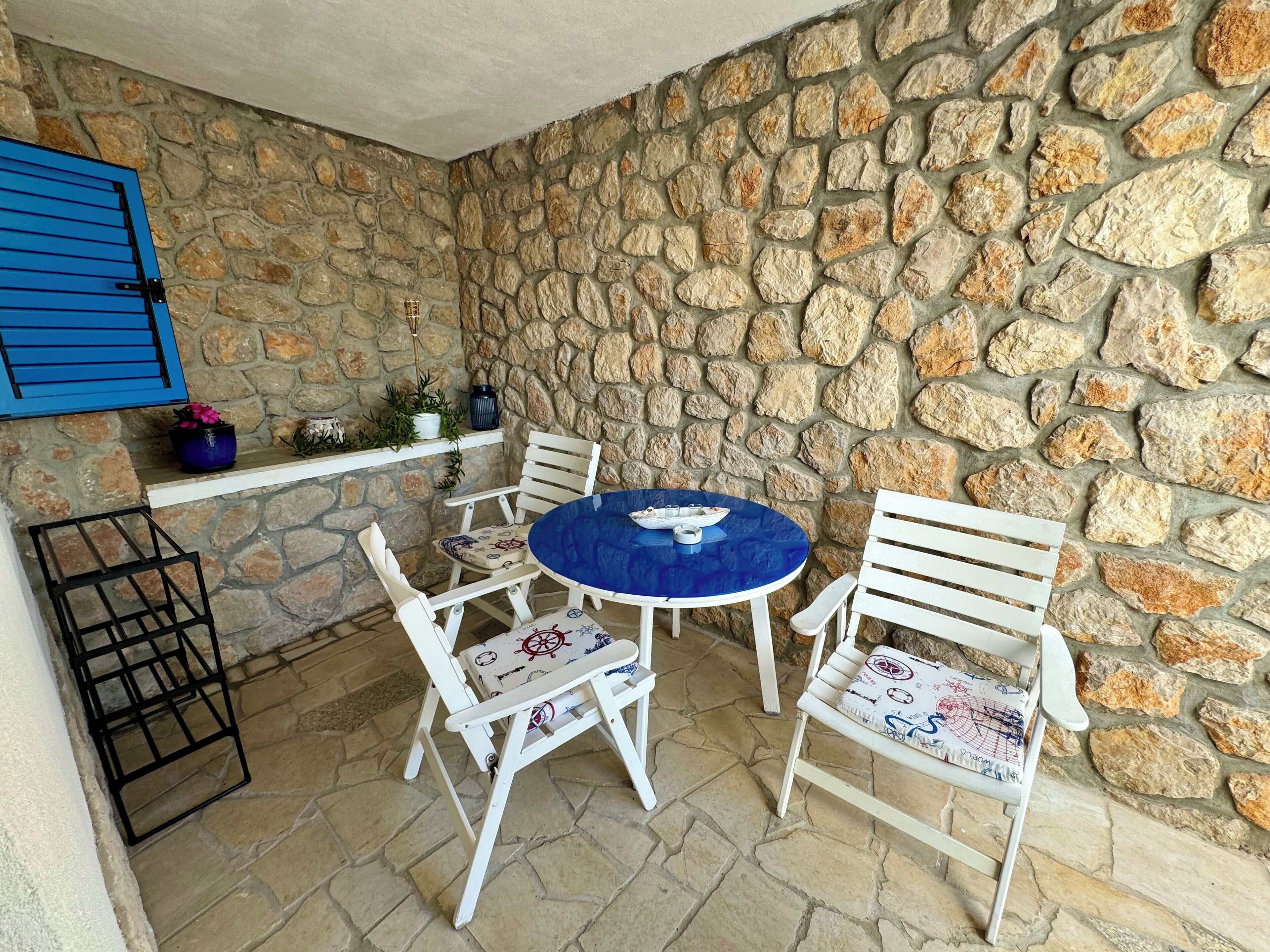 A stone-walled patio with a round table and four white chairs with patterned cushions.