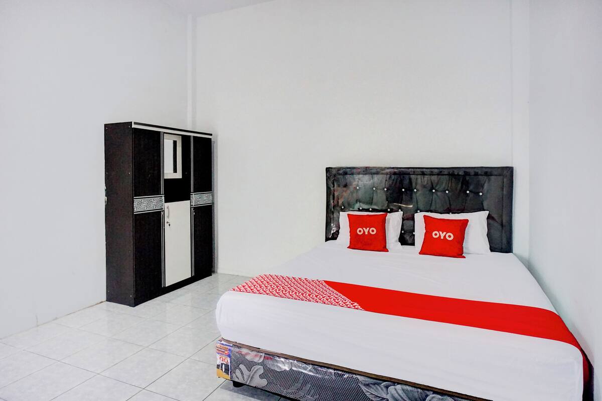 A hotel room with a bed, a wardrobe, and a red and white bedspread.