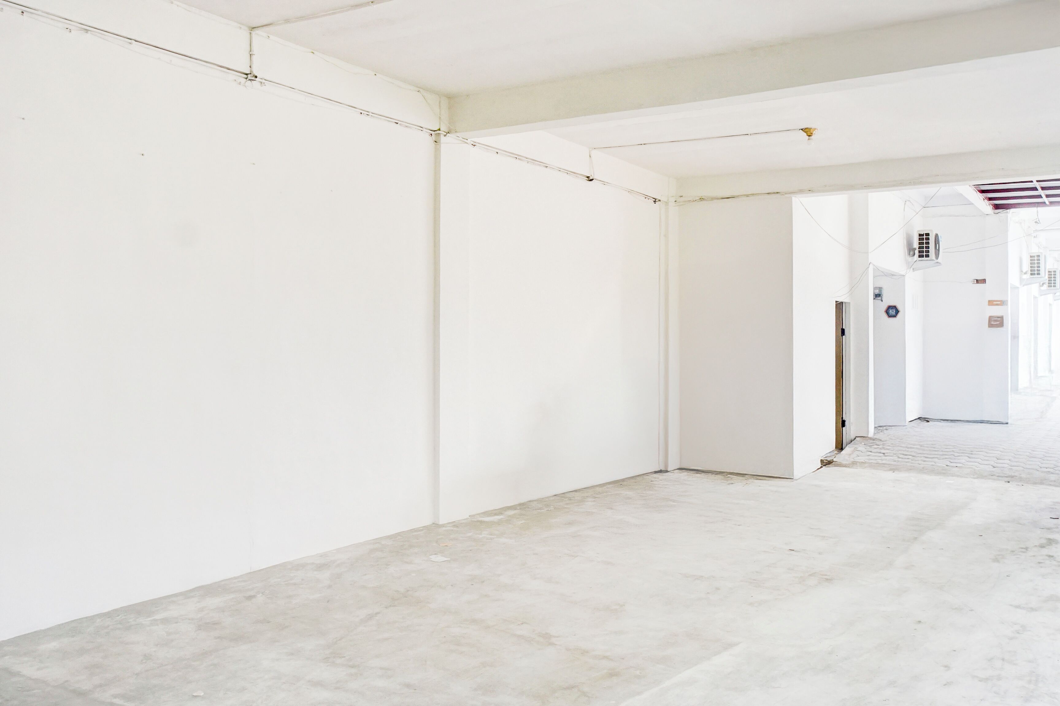 A spacious, empty hallway with white walls and a concrete floor, leading to another room.