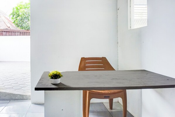 A small, modern room with a single wooden chair and a table, a potted plant on the table, and a window with blinds. - OYO 94768 Al-hamra Guest House (Medan)