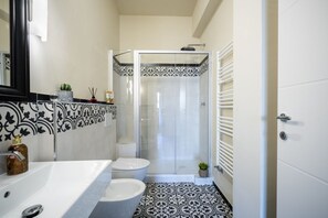 Een badkamer met een witte wastafel, toilet en douche. De vloer is betegeld met een zwart-wit patroon.