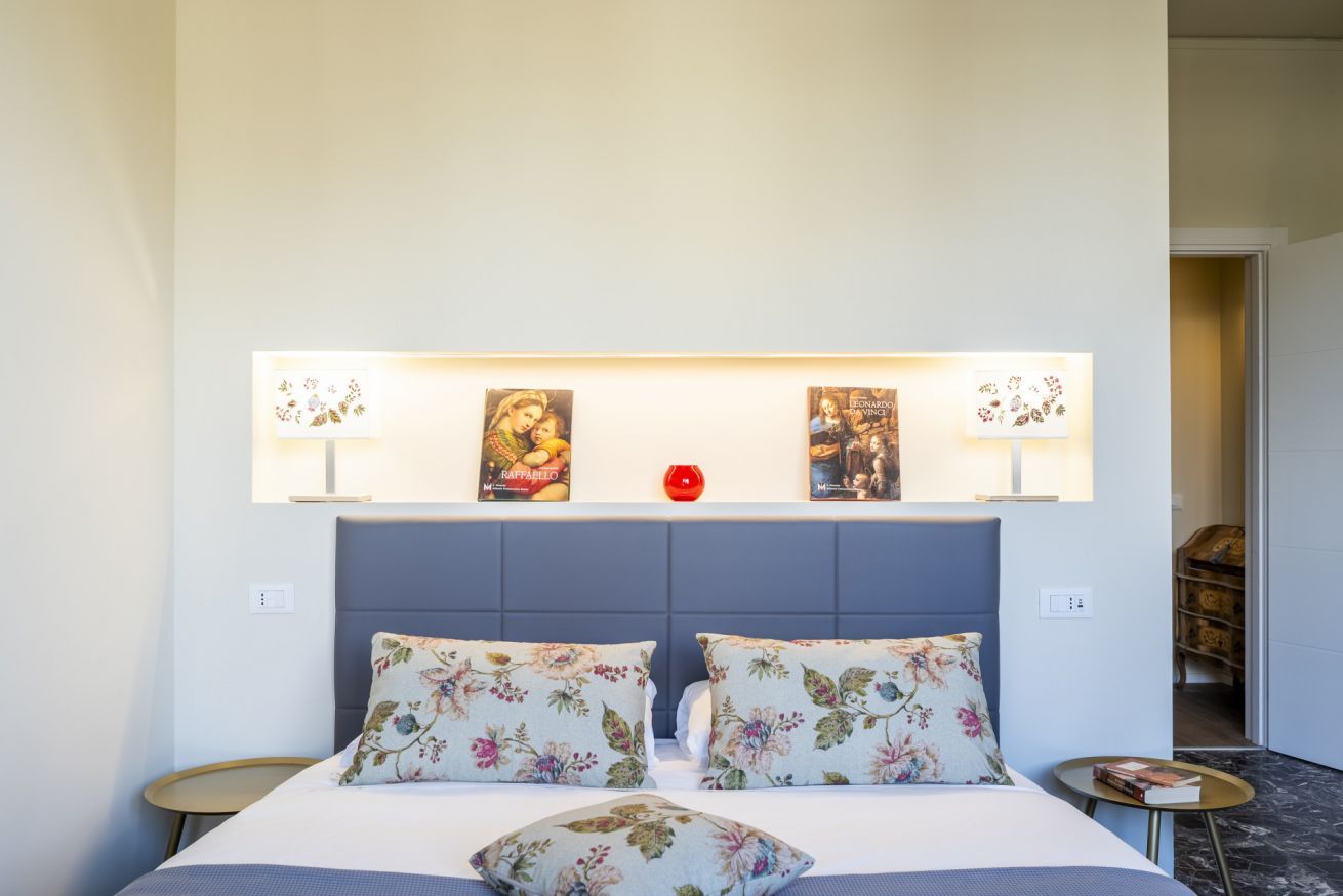 A bedroom with a bed, floral pillows, a nightstand, and wall-mounted artwork.