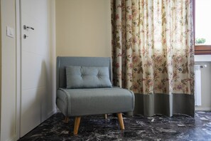 A grey sofa with wooden legs in a room with a marble floor and floral curtains. - Scena Illustrata-Redi 51-un to 10 people (Florence)
