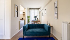 A living room with a teal sofa, a dining area with a table and chairs, and a kitchen in the background. - Illustrated Scene-Redi 51-un to 10 people (Florence)