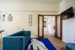 A modern living room with a blue sofa, a blue rug with a white silhouette, and a flat-screen TV mounted on the wall. - Scena Illustrata-Redi 51-un to 10 people (Florence)