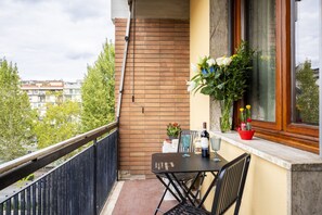 Een balkon met een tafel en stoelen, een plant in een pot en een raam met bloemen.