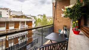 A balcony with a table and chairs, a potted plant, and a view of neighboring buildings. - Illustrated Scene-Redi 51-un to 10 people (Florence)