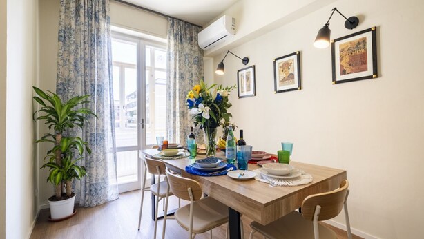 A dining area with a wooden table, chairs, a potted plant, and a vase with flowers. - Illustrated Scene-Redi 51-un to 10 people (Florence)