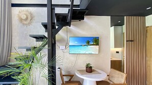 Ein modernes Zimmer mit Strandkunst an der Wand, einem runden Tisch mit zwei Stühlen, einer Topfpflanze und einer Treppe.
