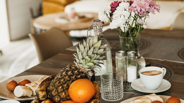 Uma mesa de café da manhã com frutas, café e um vaso de flores.