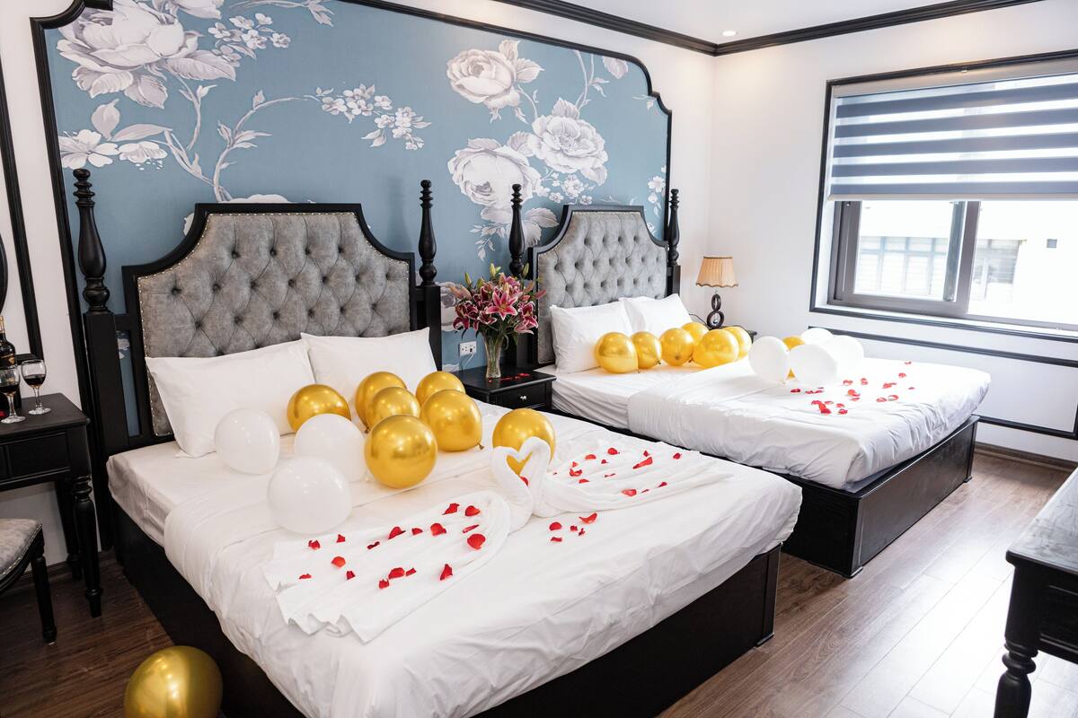 Un lit double avec du linge de lit blanc, des ballons dorés et blancs, et des pétales de rose.