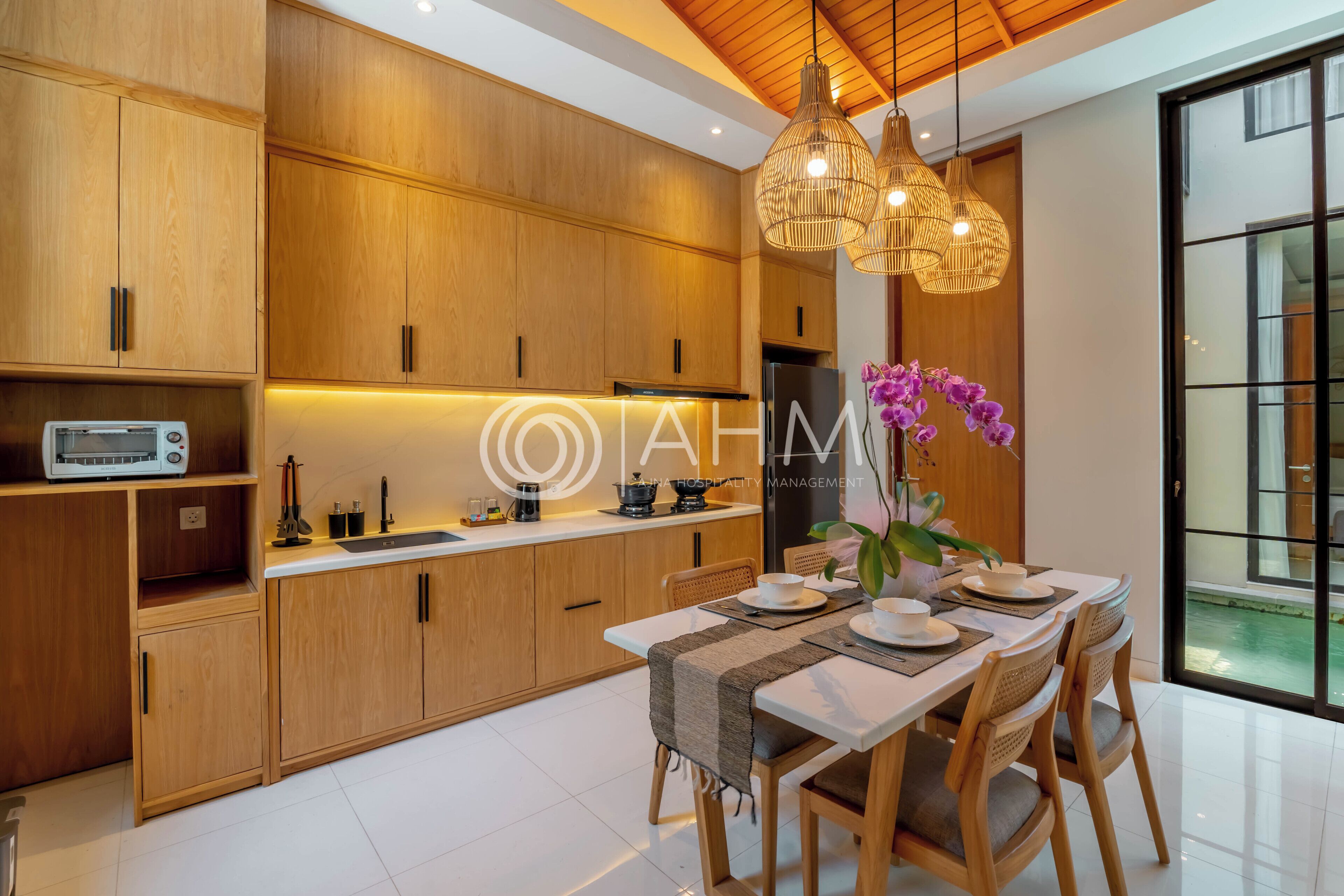 Una cucina moderna con mobili in legno, un tavolo da pranzo apparecchiato per quattro persone e vista su una piscina attraverso un'ampia finestra.