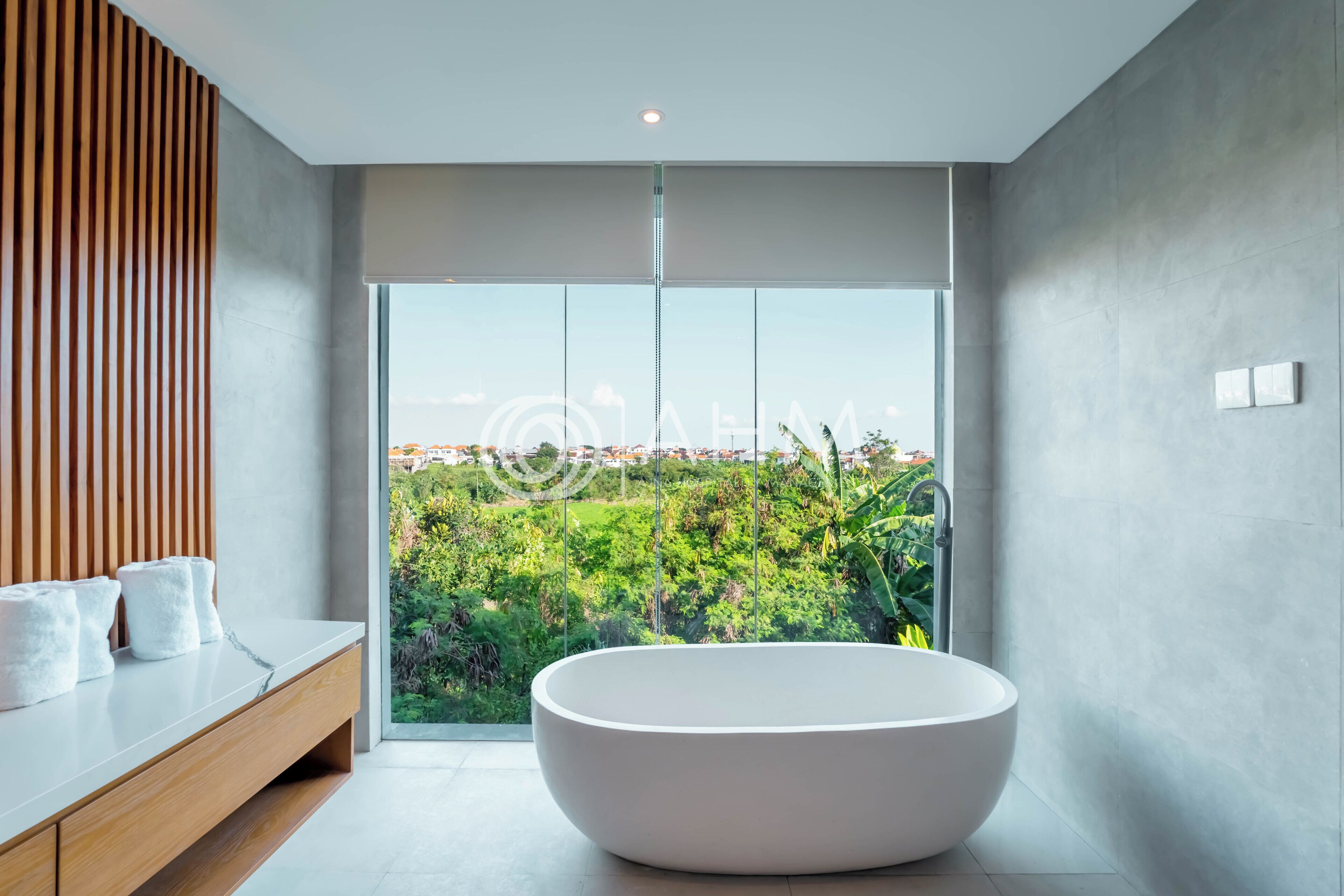A modern bathroom with a freestanding bathtub, a wooden vanity, and a large window offering a view of greenery and buildings.