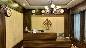 A reception area with a wooden reception desk, a chandelier, wall clocks, and a decorative tree. - Blue Poppy by Orangepetal (Gangtok)