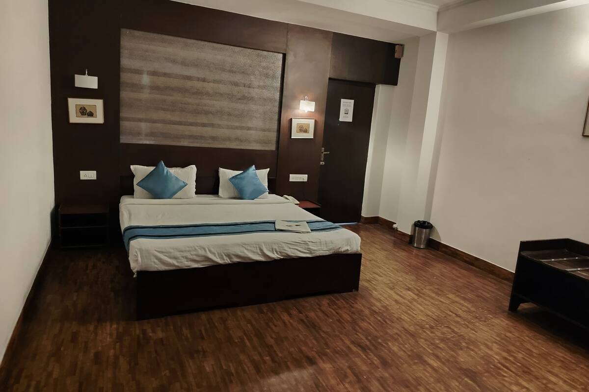 Une chambre à coucher avec un grand lit, un parquet en bois foncé et une tête de lit de couleur sombre.