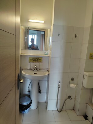 A bathroom with a sink, mirror, toilet, and shower. There is a sign advising to conserve water. - Blue Poppy by Orangepetal (Gangtok)