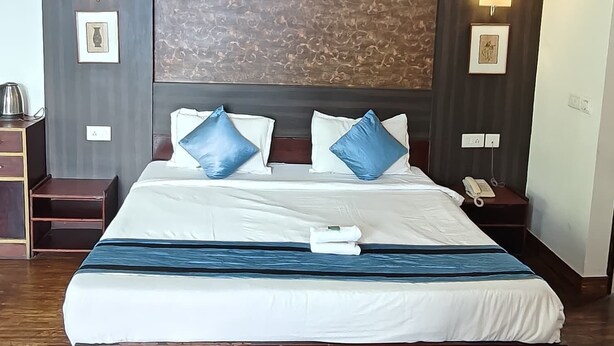 A large bed with a wooden frame, white bedding, and blue pillows. There are two bedside lamps and a telephone on a nightstand. - Blue Poppy by Orangepetal (Gangtok)