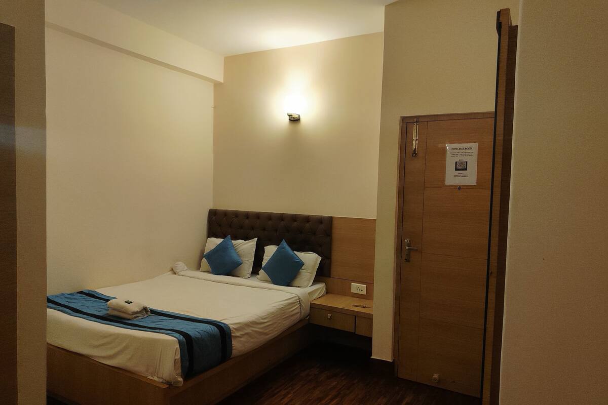 Une chambre d’hôtel avec un lit, une table de chevet, une porte en bois et une lampe fixée au mur.