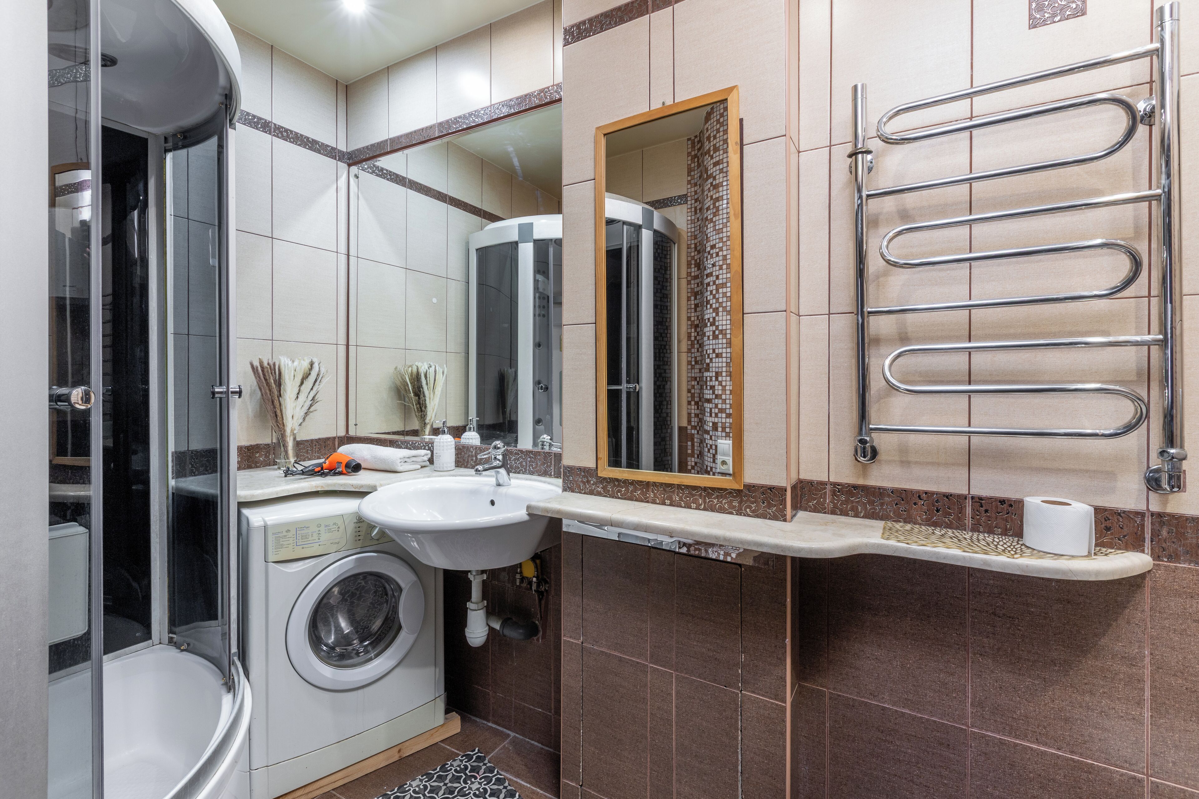 Een moderne badkamer met een ingebouwde wasmachine, een wastafel, een spiegel en een douchecabine.