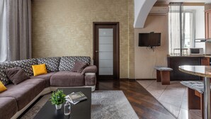A modern living room with a sectional sofa, a coffee table with a plant, and a kitchen area with a microwave. - Spacious apartment near railway station (Minsk)