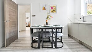 A modern kitchen with a dining area, featuring a wooden door, a white countertop, and a window.